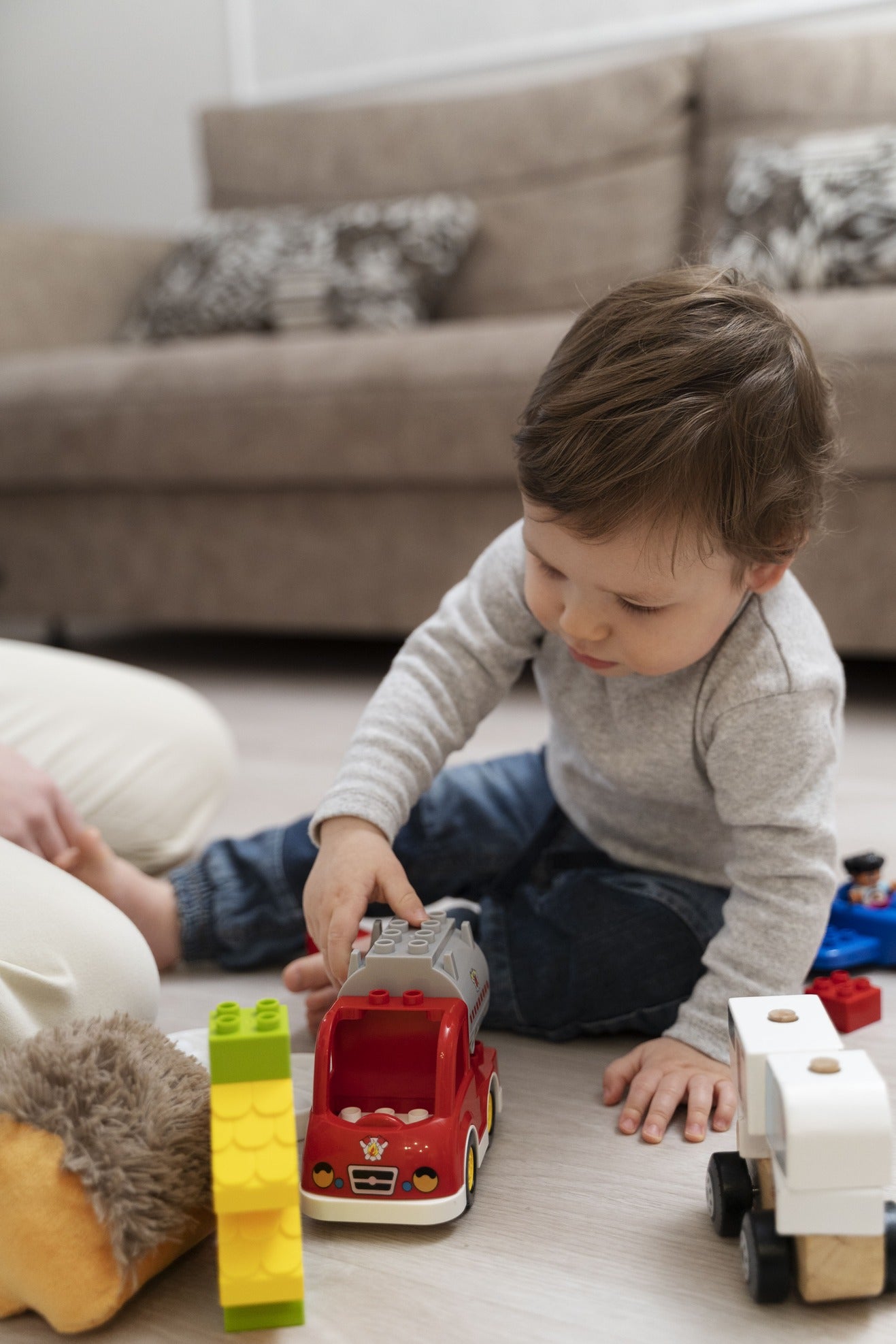 Child playing with toy cars and blocks on a light-colored floor.